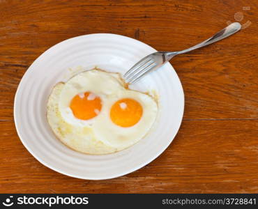 breakfast with two fried eggs on white plate on wooden table