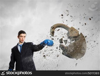 Breaking all safety measures. Young businessman in blue boxing gloves breaking stone lock