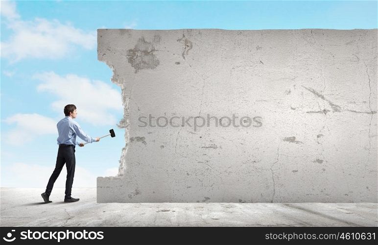 Breaking barriers. Young determined businessman breaking wall with hammer