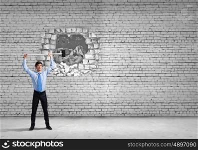Breaking barriers. Young determined businessman breaking wall with hammer
