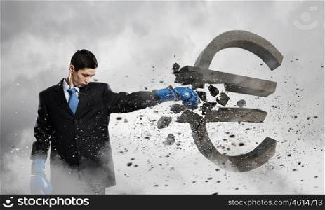 Breaking euro currency symbol. Young businessman in blue boxing gloves breaking euro sign