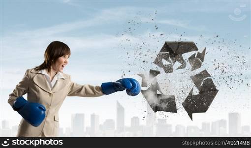 Breaking recycle concept. Young businesswoman in blue boxing gloves breaking recycle sign