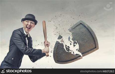 Breaking safety shield. Young emotional woman in suit and hat with baseball bat