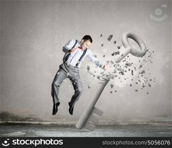 Breaking through security. Young angry businessman crashing stone key with hand