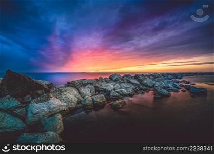 Breakwater of large rocks in the Ijsselmeer near the town of Urk in the province of Flevoland during a dramatic sunset with great clouds and colours. Impressive golden sunset at the lake