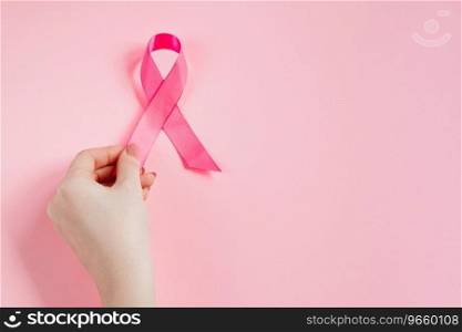 Breast Cancer Awareness Month. Woman’s hand holds pink ribbon. Health care concept, cancer control symbol. Copy space.. Breast Cancer Awareness Month. Woman’s hand holds pink ribbon. Health care concept, cancer control symbol. 