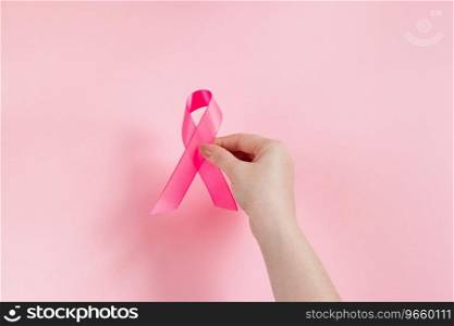 Breast Cancer Awareness Month. Woman’s hand holds pink ribbon. Health care concept, cancer control symbol. Copy space.. Breast Cancer Awareness Month. Woman’s hand holds pink ribbon. Health care concept, cancer control symbol. 