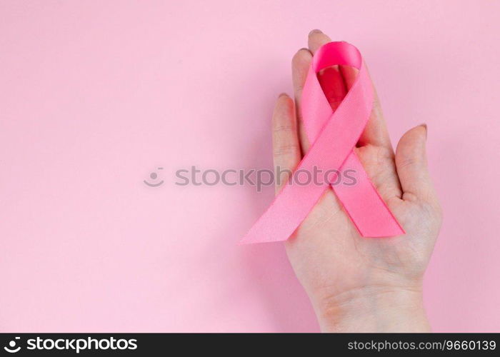 Breast Cancer Awareness Month. Woman’s hand holds pink ribbon. Health care concept, cancer control symbol. Copy space.. Breast Cancer Awareness Month. Woman’s hand holds pink ribbon. Health care concept, cancer control symbol. 