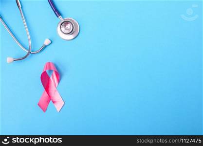 Breast cancer month concept, flat lay top view, pink ribbon and stethoscope on blue background with copy space for your text