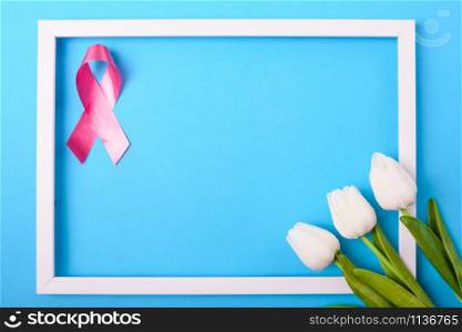 Breast cancer month concept, flat lay top view, pink ribbon and Tulip Flower with photo frame on blue background with copy space for your text