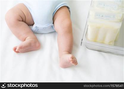 Breast milk frozen in storage bag and leg infant baby lying on white bed