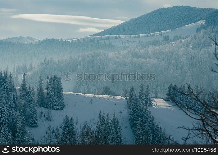 Breathtaking winter mountain landscape covered with snow, forests in the misty distant backdrop. Picturesque and peaceful wintry scene European resort location. Sunny day with clouds