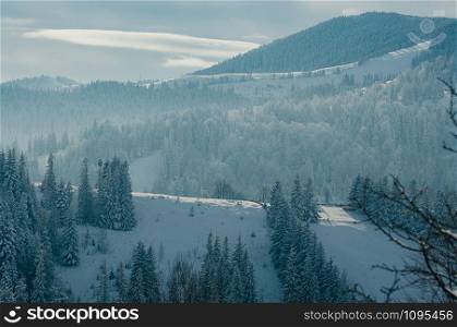 Breathtaking winter mountain landscape covered with snow, forests in the misty distant backdrop. Picturesque and peaceful wintry scene European resort location. Sunny day with clouds
