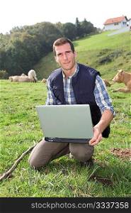 Breeder sitting in cattle field with laptop computer