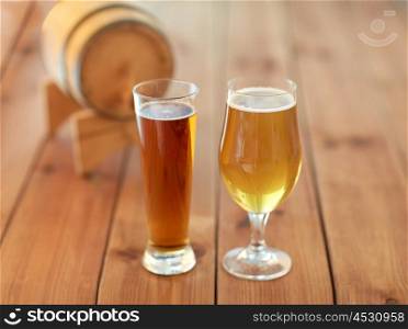 brewery, drinks and alcohol concept - close up of different beers in glasses and barrel on wooden table