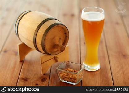 brewery, drinks and alcohol concept - close up of draft lager beer in glass, peanuts and wooden barrel on table
