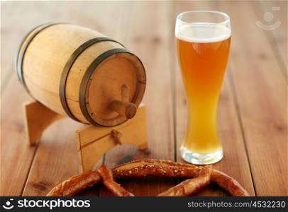 brewery, drinks and alcohol concept - close up of draft lager beer in glass, pretzel and wooden barrel on table