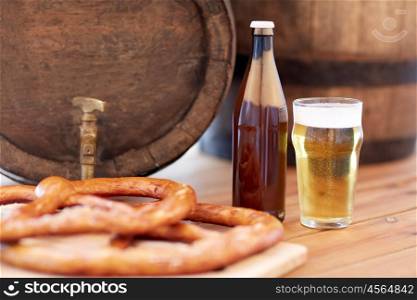 brewery, drinks and alcohol concept - close up of old beer barrel, glass, bottle and pretzel on wooden table