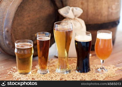 brewery, drinks and alcohol concept - close up of old beer barrel, glasses and bag with malt on wooden table