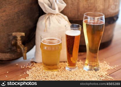 brewery, drinks and alcohol concept - close up of old beer barrel, glasses and bag with malt on wooden table