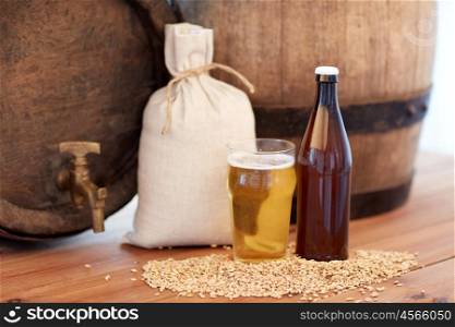 brewery, drinks and alcohol concept - close up of old beer barrel, glass, bottle and bag with malt on wooden table