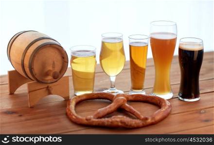 brewery, drinks and food concept - close up of different beer glasses, wooden barrel and pretzel on table