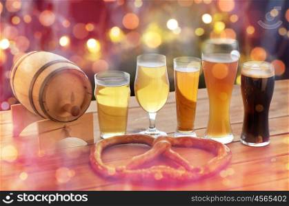brewery, drinks and food concept - close up of different beer glasses, wooden barrel and pretzel on table over holidays lights background