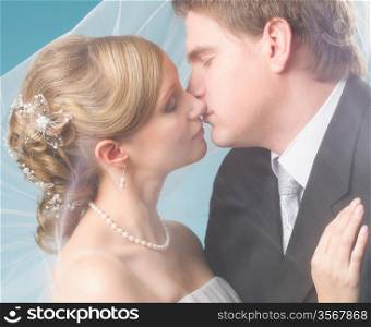 Bridal couple kissing under a veil, blue background