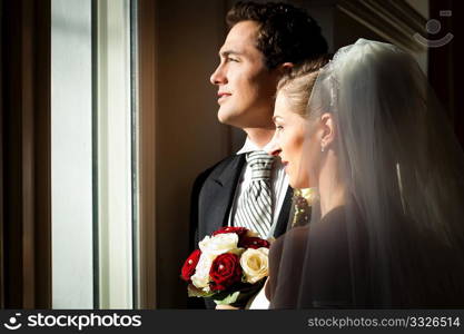 Bridal couple standing at the window at their wedding and looking outside