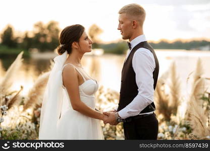 bride and groom against the backdrop of a yellow sunset on a pier near the river