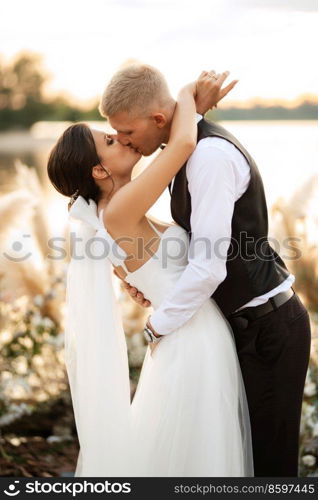 bride and groom against the backdrop of a yellow sunset on a pier near the river