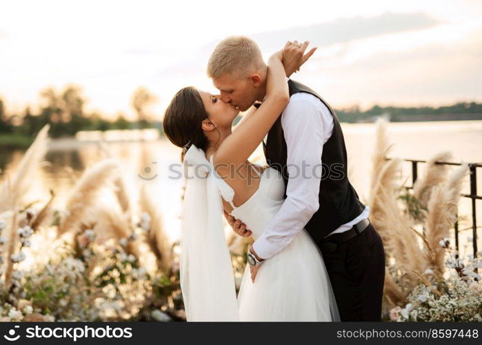 bride and groom against the backdrop of a yellow sunset on a pier near the river