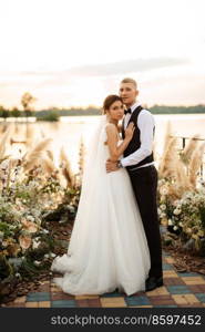 bride and groom against the backdrop of a yellow sunset on a pier near the river