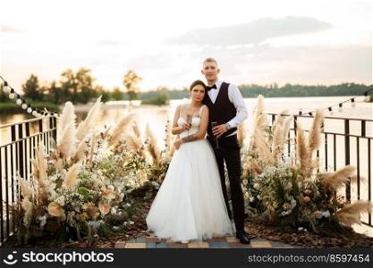 bride and groom against the backdrop of a yellow sunset on a pier near the river
