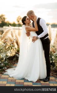 bride and groom against the backdrop of a yellow sunset on a pier near the river