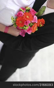 Bride and groom are holding each other with a bouquet of flowers in between them.