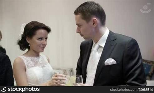 Bride and groom clanging glasses and talking. Beautiful bride is very emotional and excited.