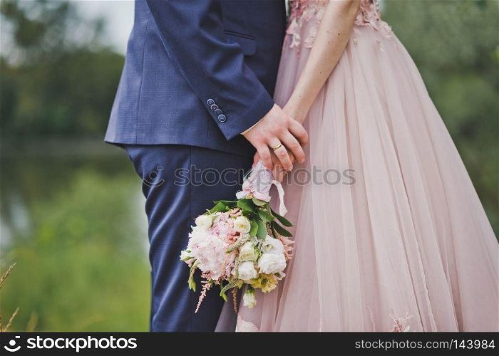 Bride and groom holding a bouquet of flowers.. A bouquet of flowers in hands of the newlyweds on a walk through natur