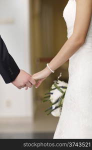 Bride and groom holding hands as they stand making their vows of love and commitment, closeup view of their clasped hands