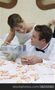 Bride and groom relaxing on bed among presents, portrait