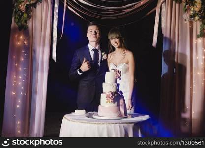 bride and groom stand next to a large wedding cake outside. wedding day.. bride and groom stand next to a large wedding cake outside. wedding day