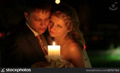 bride and groom standing embraced at night holding in hands burning candle