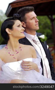Bride and groom standing side by side outdoors, smiling, portrait
