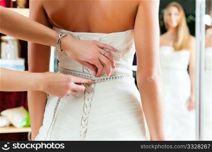 Bride at the clothes shop for wedding dresses; she is choosing a dress and the designer is assisting her
