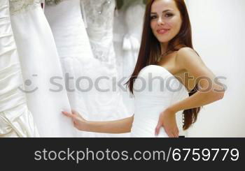 Bride choosing wedding dress in bridal boutique, smiling, looking at camera
