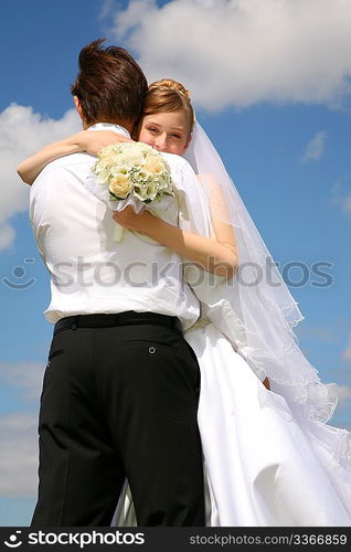 bride embraces fiance against the background of the sky