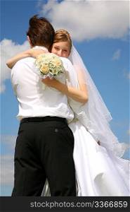 bride embraces fiance against the background of the sky