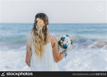 Bride facing the sea with colorful flowers in hand