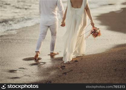 Bride groom walking on choppy Beach, bride has flowers in her hand