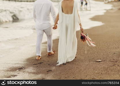 Bride groom walking on choppy Beach, bride has flowers in her hand